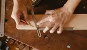 Hands using a square to mark a line on a wooden board on a workbench.