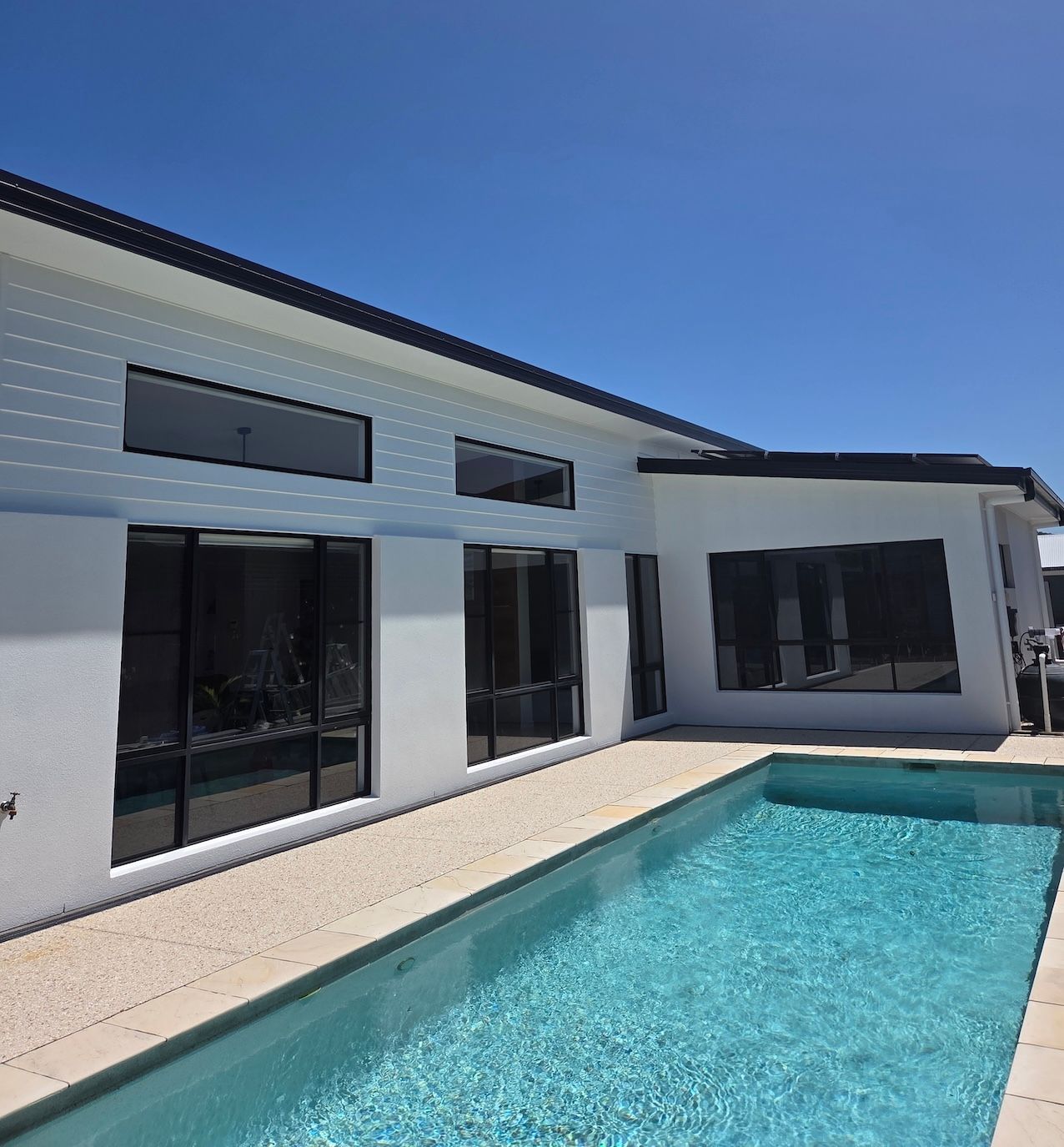 White house with large dark-tinted windows, and a rectangular pool on a sunny day— MVP Painting Professionals in Sunshine Coast, QLD