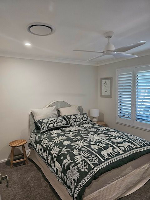 Bedroom With a Bed Covered in a Dark Floral Pattern, Shutters, and a Stool — MVP Painting Professionals in Caloundra, QLD