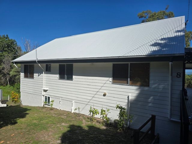 A white, single-story house with a grey corrugated metal roof, number 8 on the side, surrounded by a lawn and trees— MVP Painting Professionals in Sunshine Coast, QLD