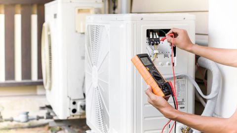 Technician testing an outdoor AC unit with a multimeter and removing its cover