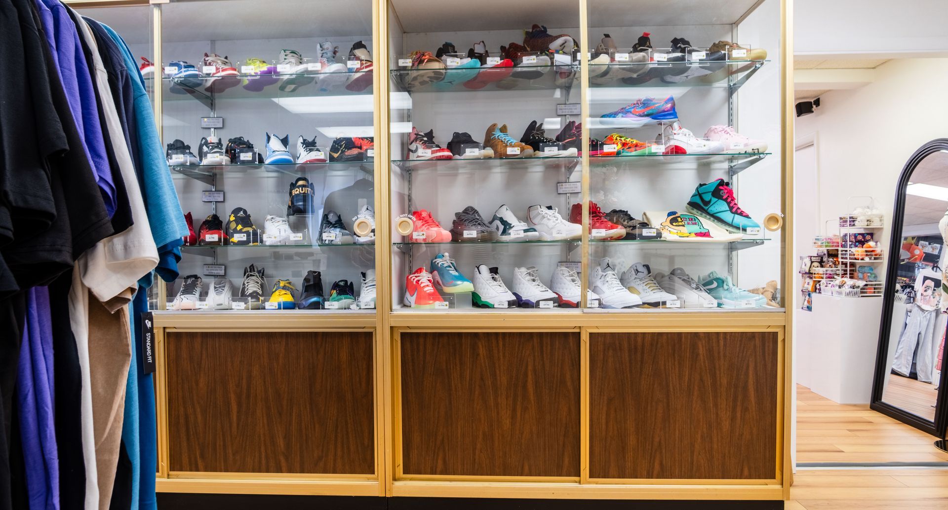 Shoe store display with rows of sneakers on glass shelves and folded clothes on the left.