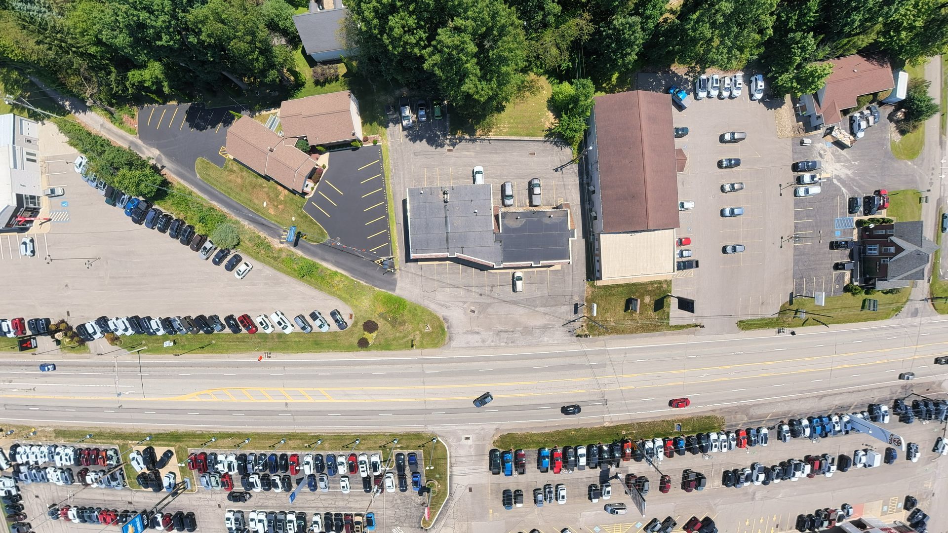 Aerial view of a parking lot, buildings, and a road with cars along the bottom edge.
