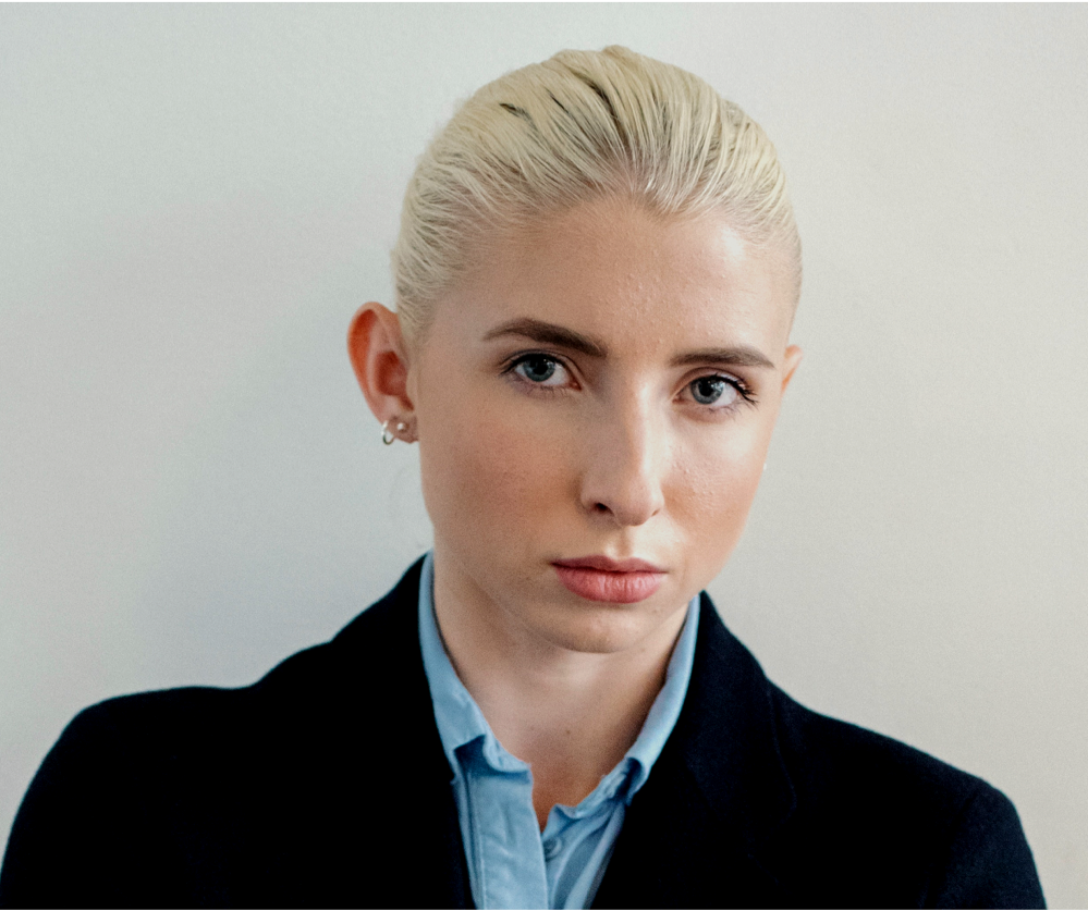 Una mujer con cabello rubio lleva una camisa azul y una chaqueta negra.