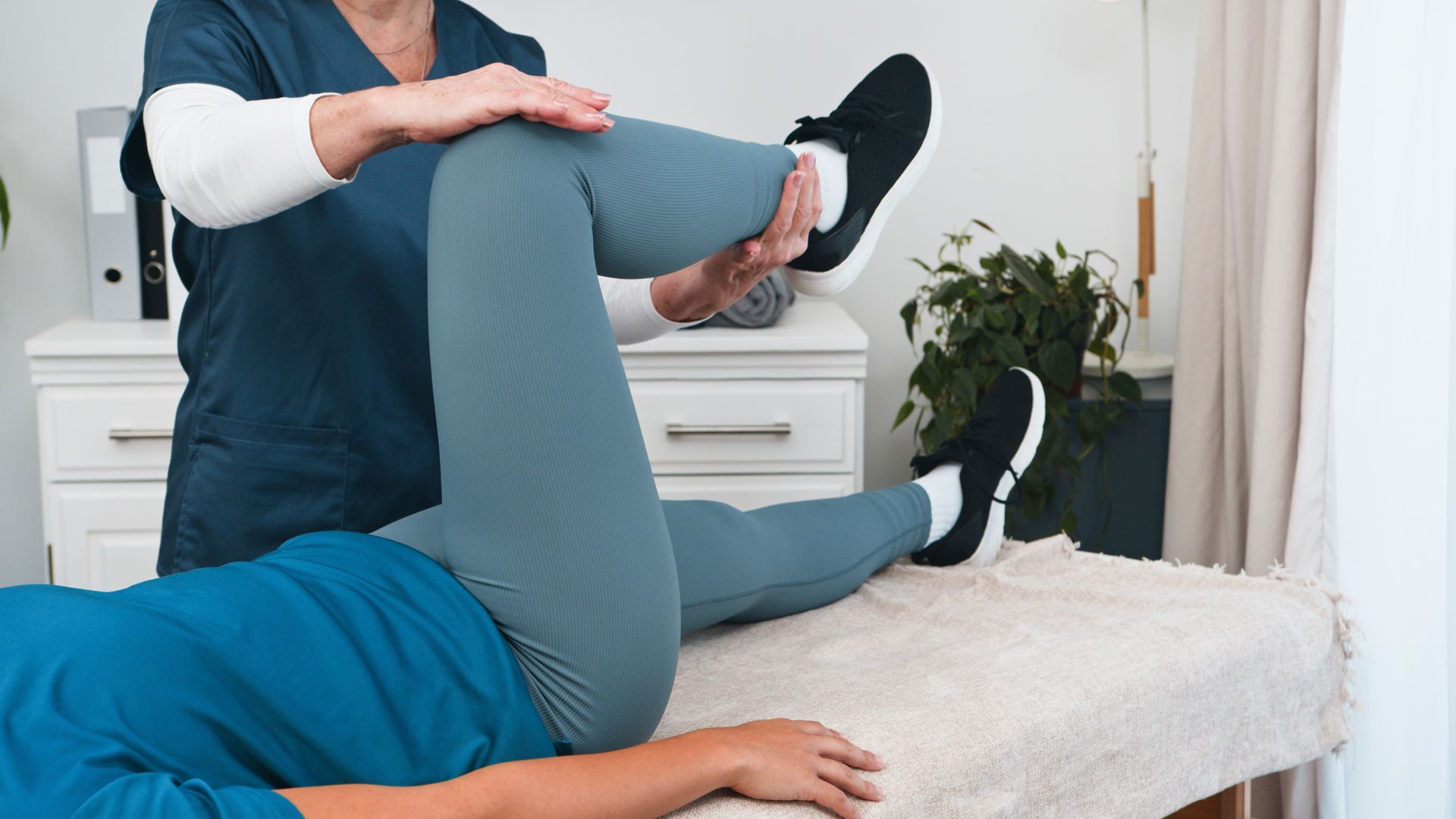 Physical therapist stretching a patient’s leg on a massage table in a bright treatment room