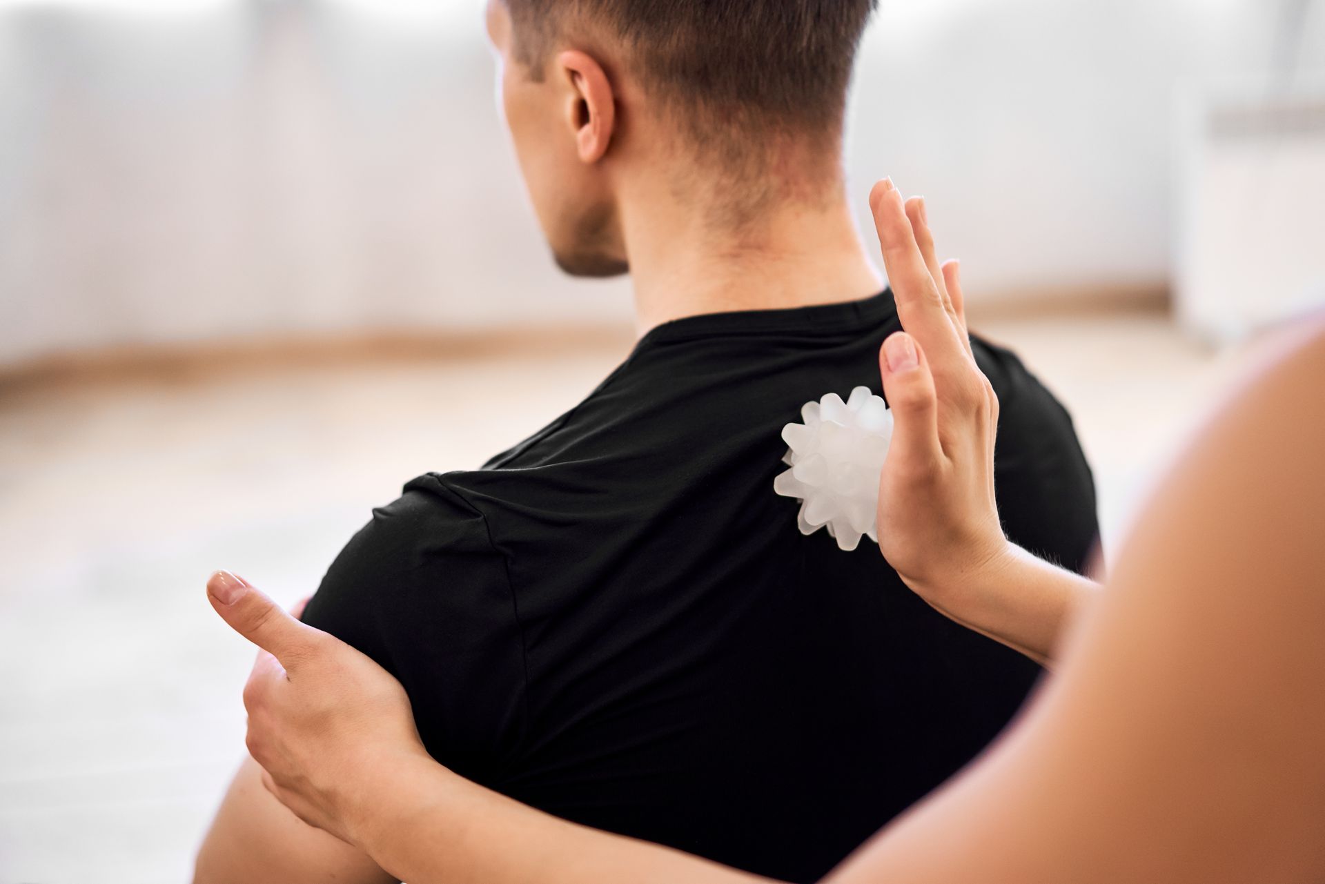 Person applying white cream to a man’s upper back and shoulder during a massage treatment