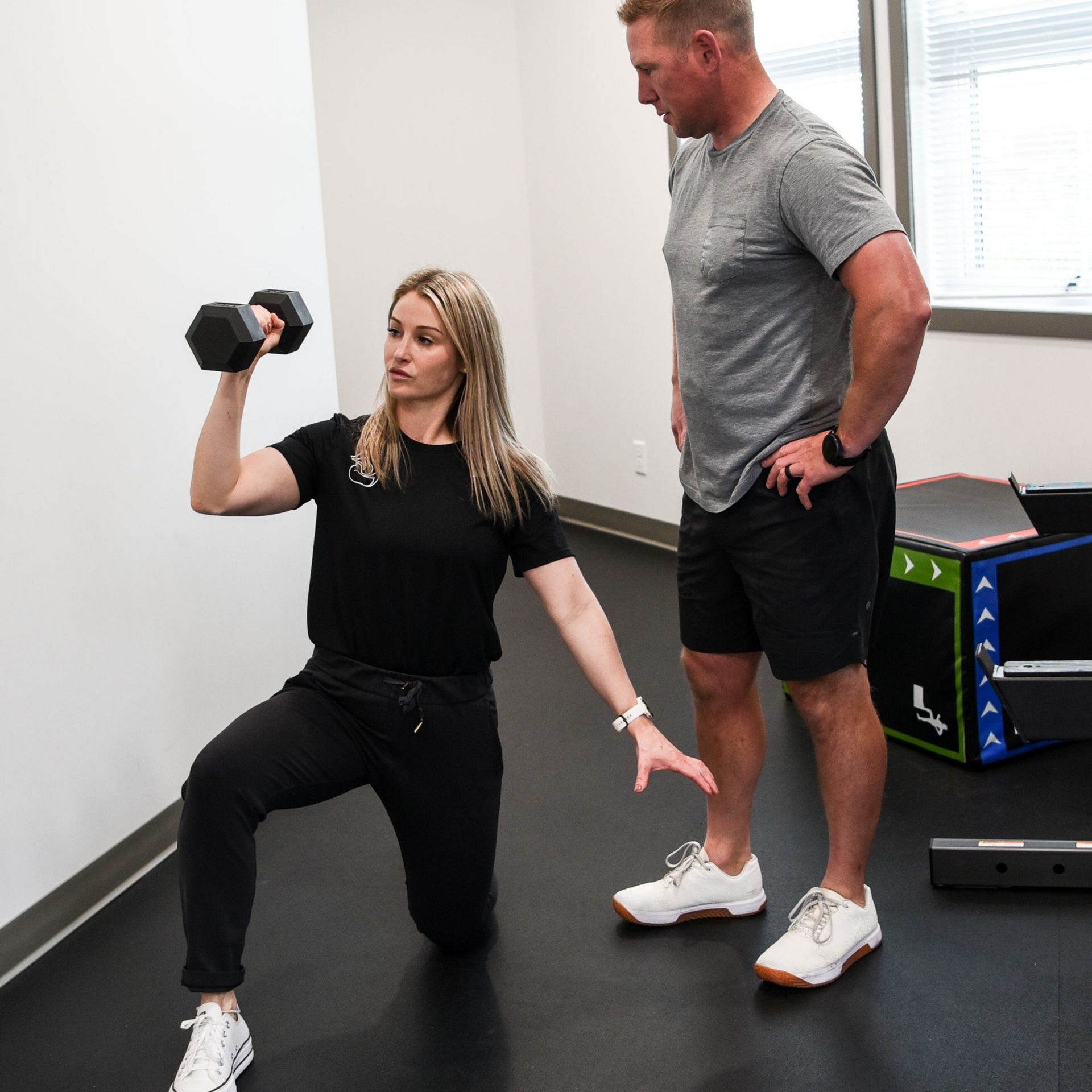 Woman doing a dumbbell lunge while a trainer watches in a gym