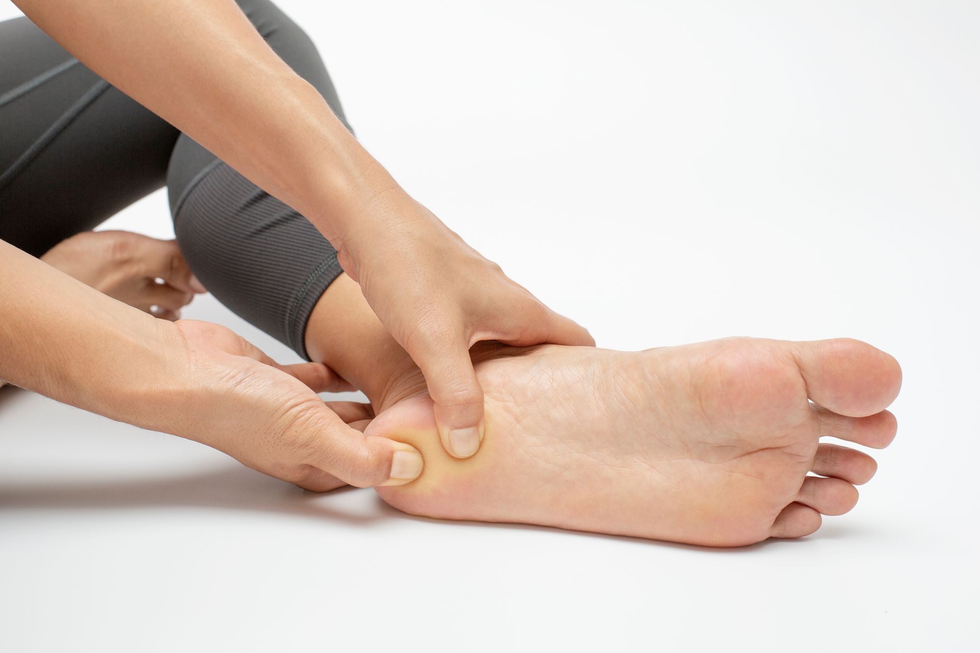 Hands massaging a bare foot and ankle on a white background