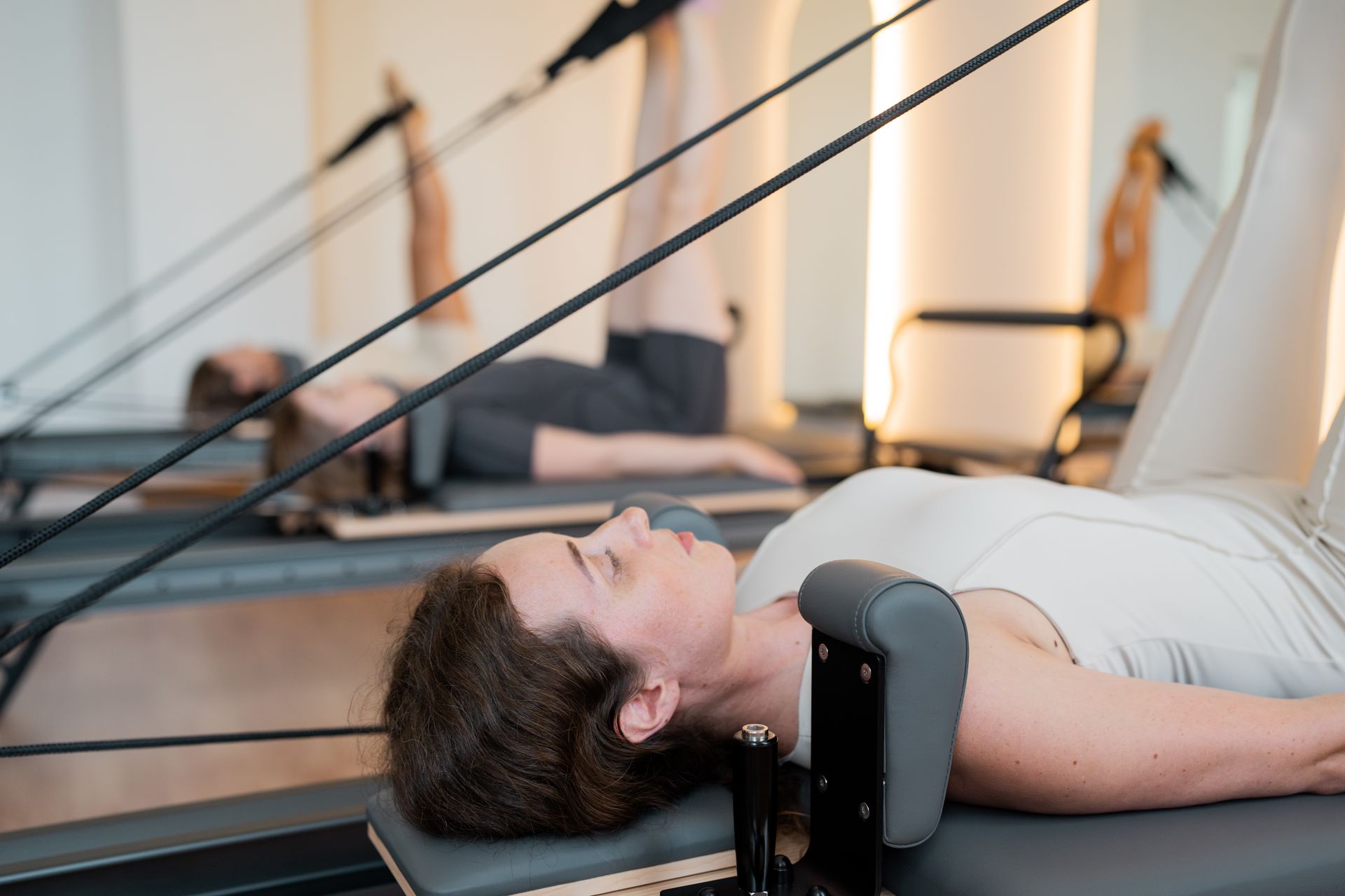 Person lying on a Pilates reformer, doing a core exercise with black resistance straps in a studio