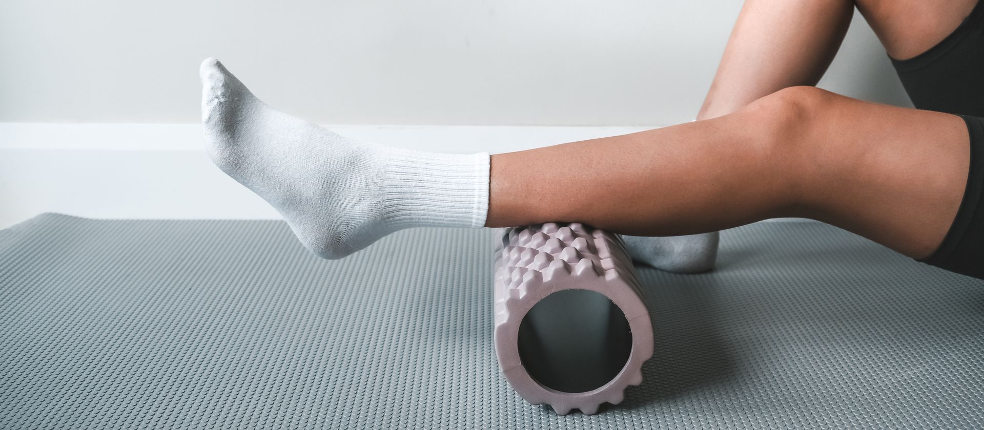 Person stretching a calf over a foam roller on a gray mat