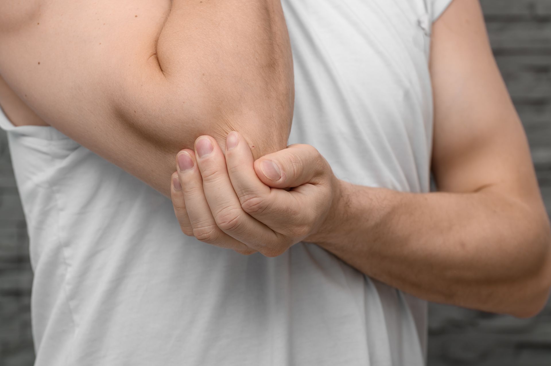 Person holding an injured elbow with the other hand against a gray background