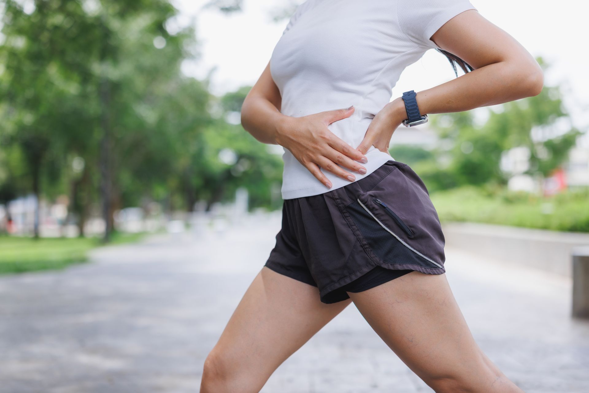 Person jogging outdoors on a tree-lined path, wearing a white shirt and black shorts.