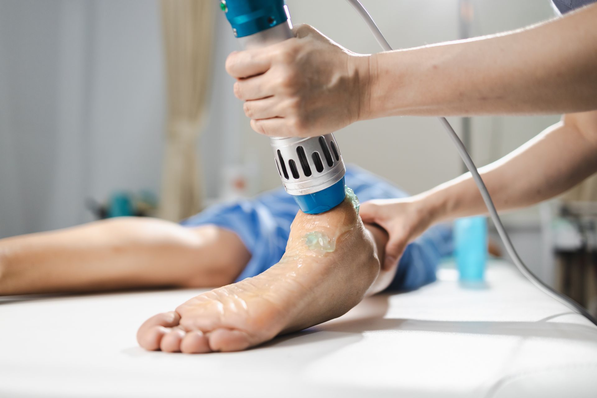 Therapist using a handheld device on a patient’s ankle during a treatment session