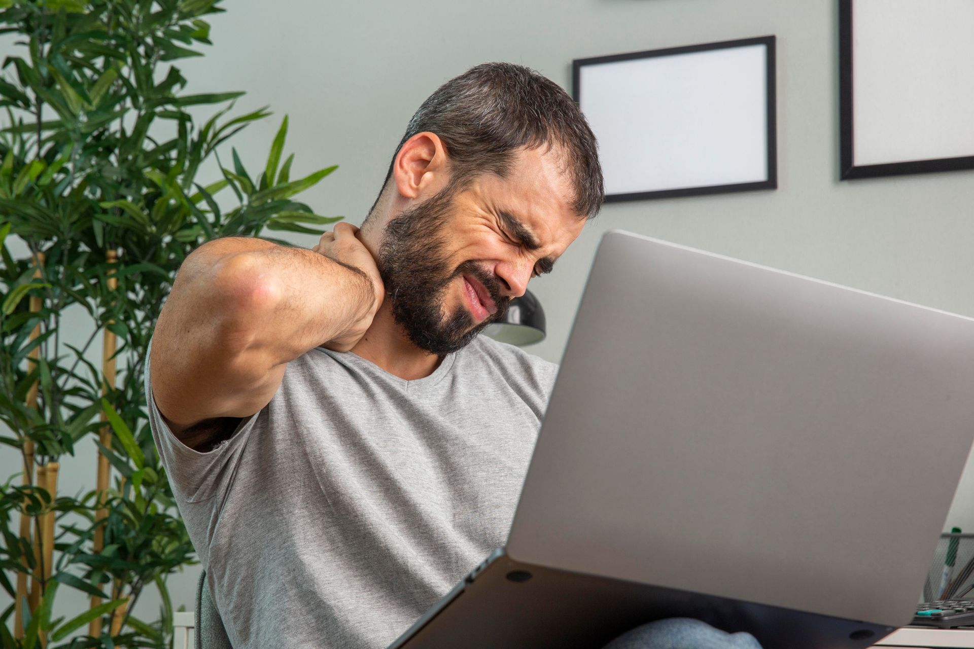 Man rubbing his neck while using a laptop in a bright room