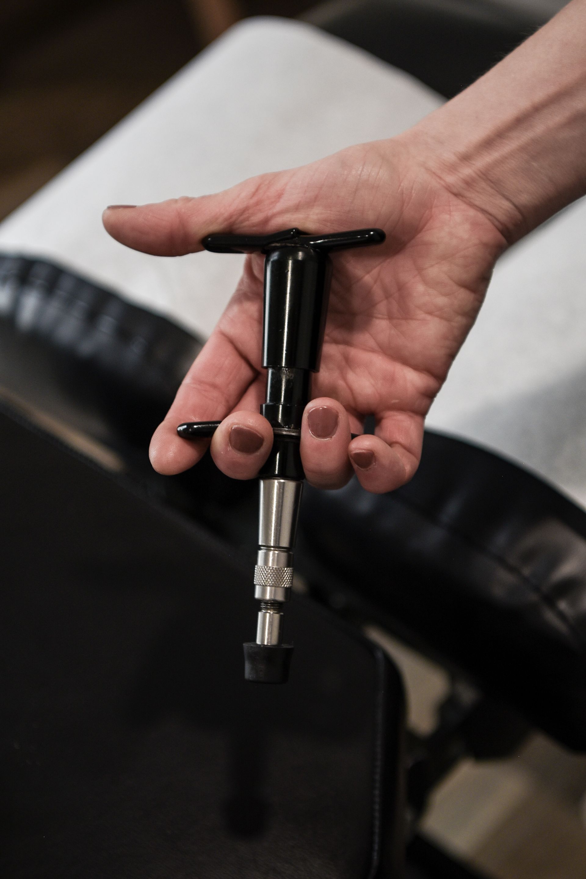 Hand holding a black chiropractic adjusting tool above a black treatment table.