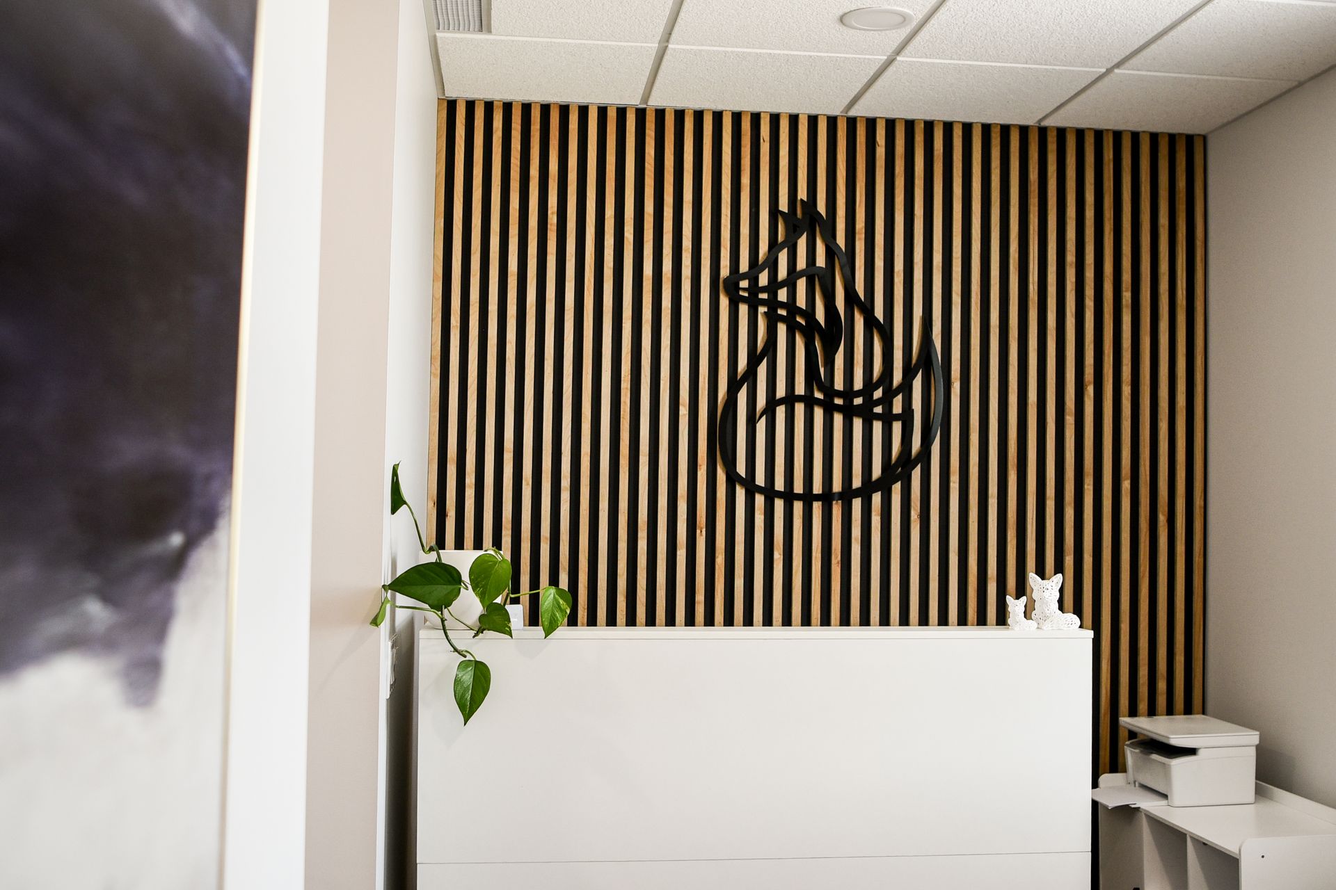 Reception desk with wooden slat wall, black logo, and white desk with plant.