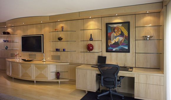 Modern home office with built-in shelves, TV, desk, black chair, and colorful wall art