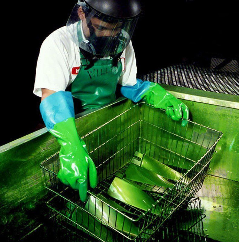 Worker in green gloves and apron cleaning a wire basket in a sink with green liquid