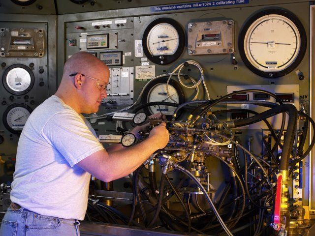 Technician adjusting wiring and gauges in a laboratory control room with vintage instruments