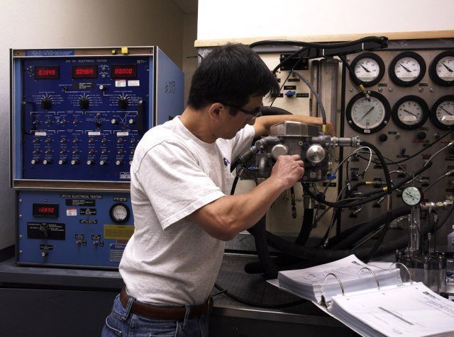 Technician adjusting gauges on industrial equipment beside a blue control panel in a lab.