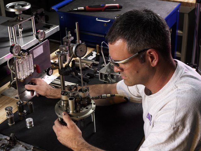 Technician adjusting a mechanical device at a workbench in a workshop, with tools and instruments nearby