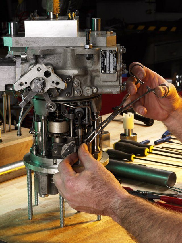 Hands using a screwdriver to repair a metal engine or machinery on a workbench