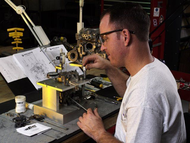 Man working with a small machine on a cluttered workbench in a workshop