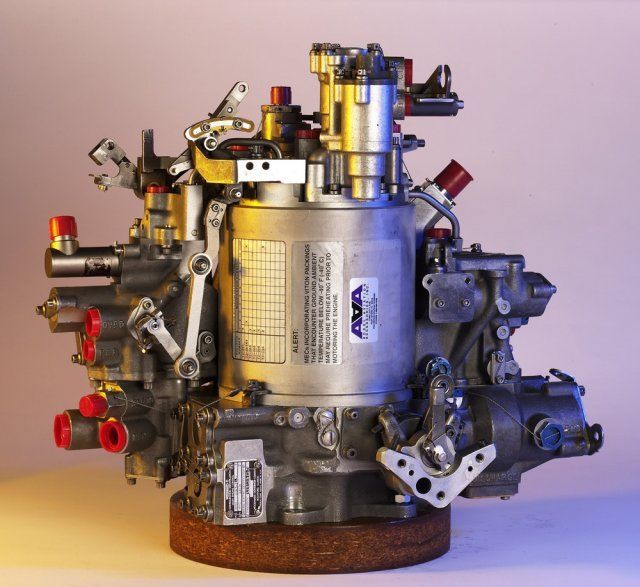 Industrial engine component with metal housing, hoses, and fittings on a plain background