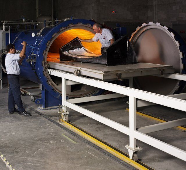 Two workers loading a large glowing furnace drum in an industrial workshop
