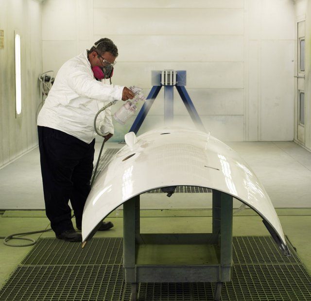 Worker spraying a large white aircraft part in a paint booth