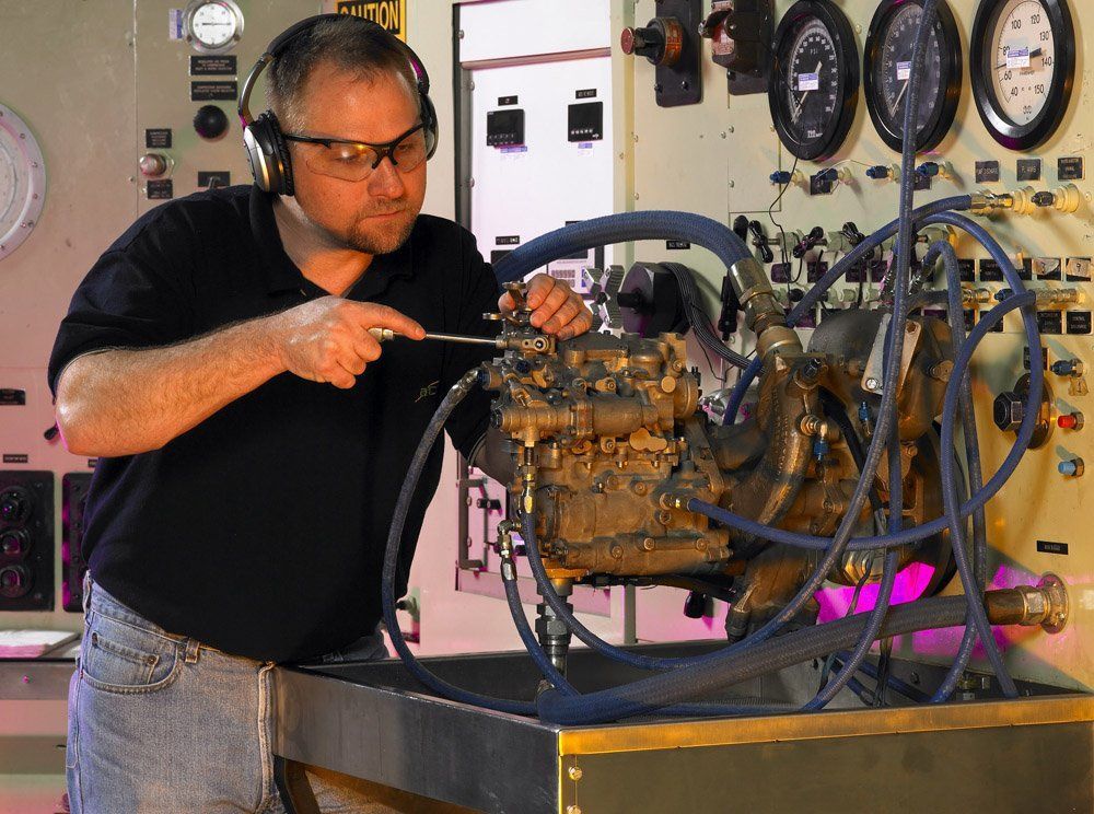 Technician inspecting a diesel engine with gauges and hoses in a workshop lab