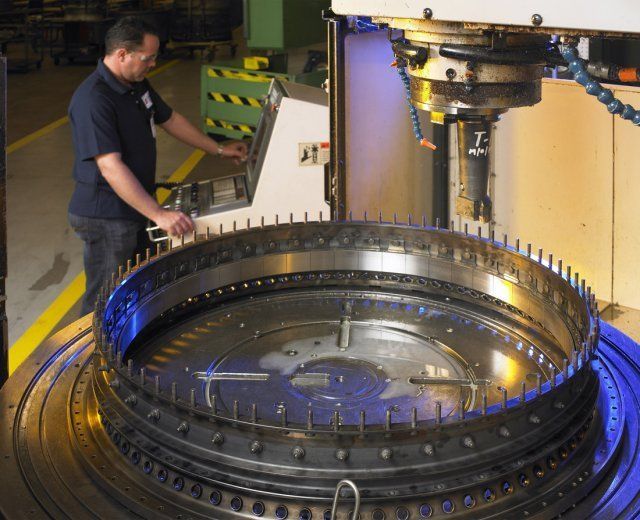 Worker operating a large industrial machine with a circular metal platform in a factory.