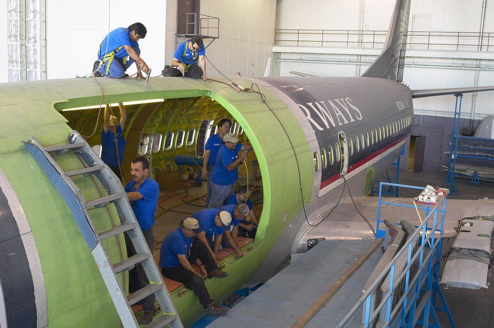 Workers inside a large green aircraft fuselage section in a factory assembly area