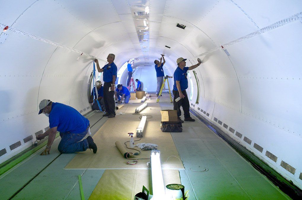 Workers in blue coveralls wiring a bright white cylindrical tunnel interior.