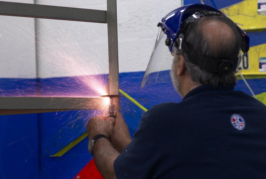 Worker welding a metal frame, sparks flying, wearing a face shield in a workshop