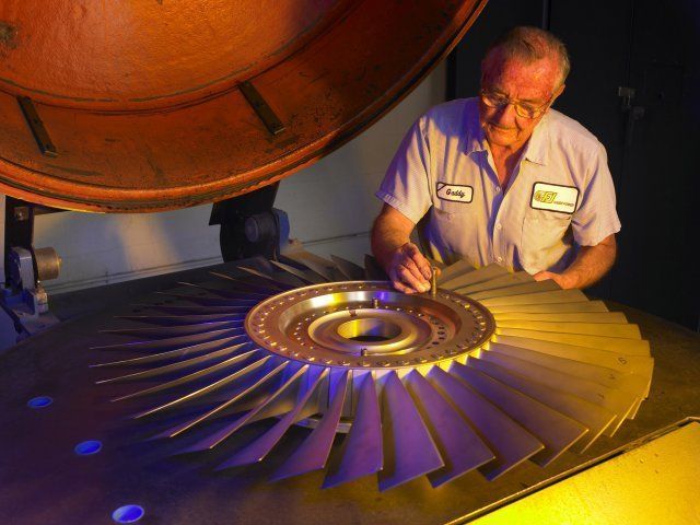 Technician inspecting a turbine blade under warm light in an industrial workshop