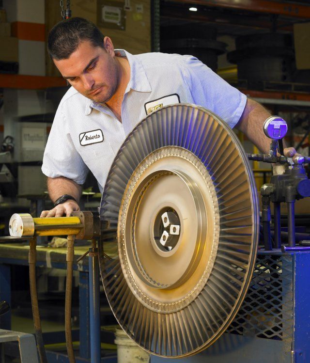 Worker using a large grinding wheel in a workshop, leaning over the machine and focused on the task