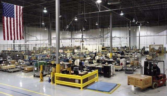 Large aircraft assembly factory with machinery and workstations, under a hanging American flag