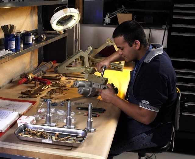 Mechanic working on a bicycle at a cluttered repair bench under a lamp