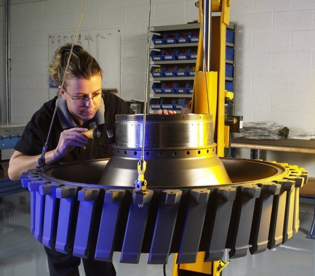 Technician inspects a large industrial machine in a workshop, with blue and yellow machinery parts visible.