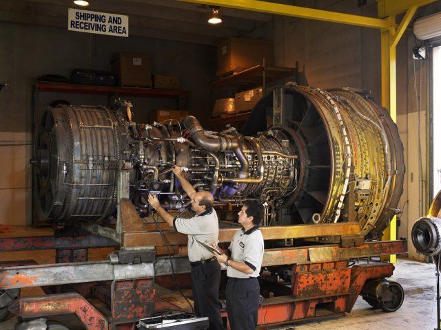 Workers inspect a large jet engine in an industrial maintenance bay