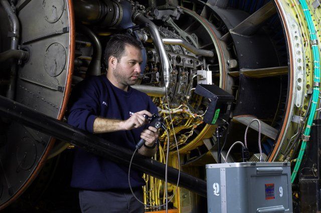 Technician inspecting machinery with a cable inside a large industrial engine compartment