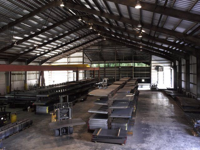 Empty industrial warehouse with stacks of metal beams under a large steel roof.