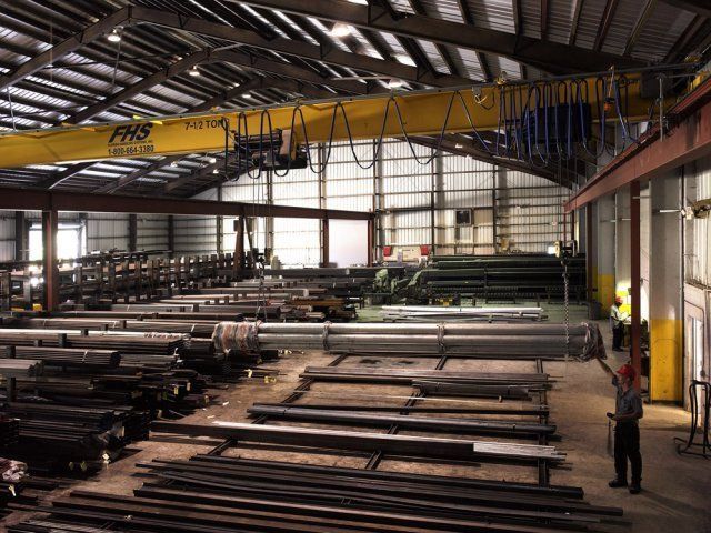 Interior of a steel warehouse with stacked metal beams and a yellow overhead crane overhead