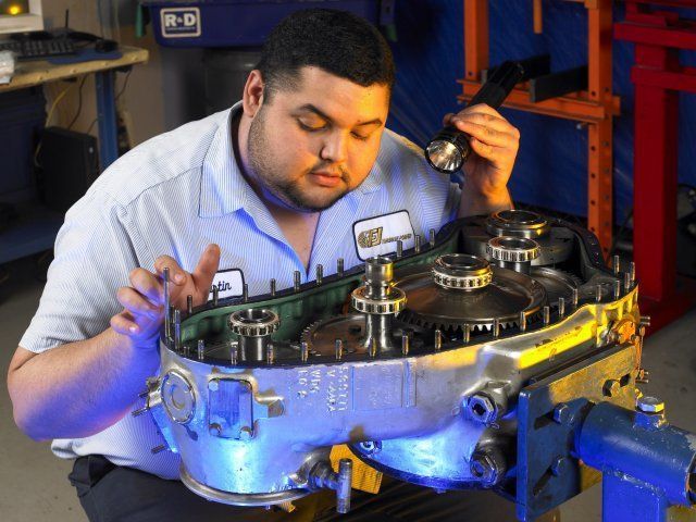 Mechanic inspecting a car transmission on a workbench with tools in a garage