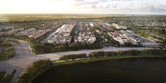 Aerial view of a suburban neighborhood with roads, trees, and a dark lake in the foreground at sunset