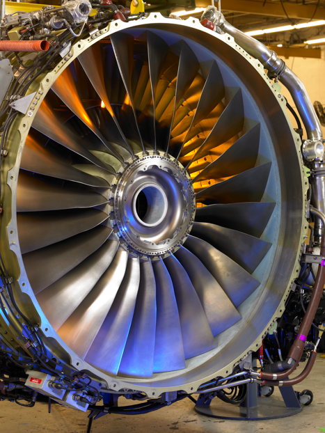 Close-up of a jet engine turbine with metallic fan blades and a blue-lit center in a workshop.