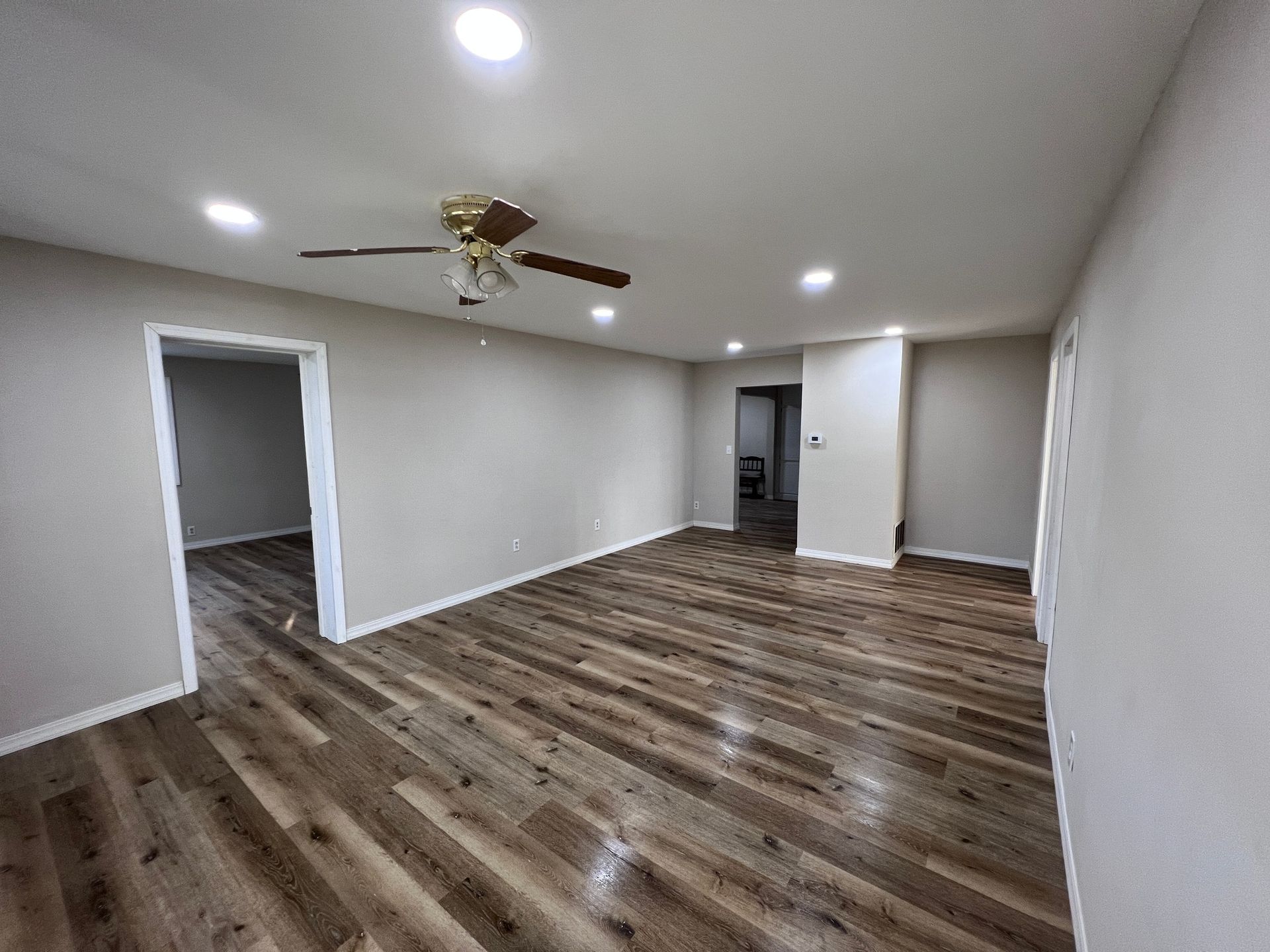 Empty living room with wood-look flooring, light gray walls, recessed lighting, and a ceiling fan.