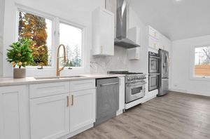 White kitchen with stainless steel appliances, white cabinets, and a window overlooking trees.
