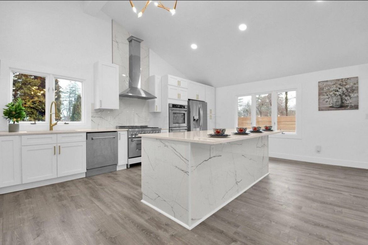 Modern white kitchen with island and stainless steel appliances; hardwood floors.